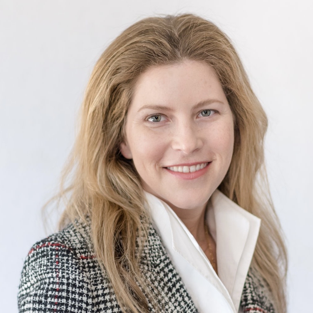 A smiling headshot of a woman with blonde hair, wearing a plaid blazer over a white blouse, against a white background.